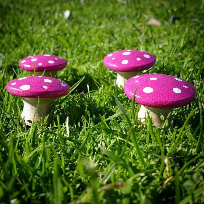 May include: Five pink and white mushroom shaped decorations with white polka dots. The mushrooms are sitting on a bed of green grass.