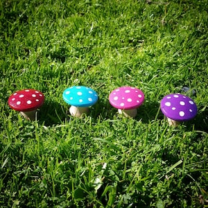 May include: Four painted wooden mushrooms with white polka dots. The mushrooms are painted in shades of pink, blue, purple, and red.