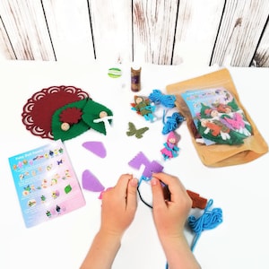 May include: A craft kit for making felt fairy dolls. The kit includes felt pieces, yarn, glue, and instructions. The image shows a person assembling a fairy doll.