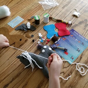 May include: A child is sewing a gray felt horse with white yarn. The horse has white felt for its mane and tail. The kit includes felt pieces, yarn, needles, and instructions. The instructions are titled "Horse Sewing Kit".