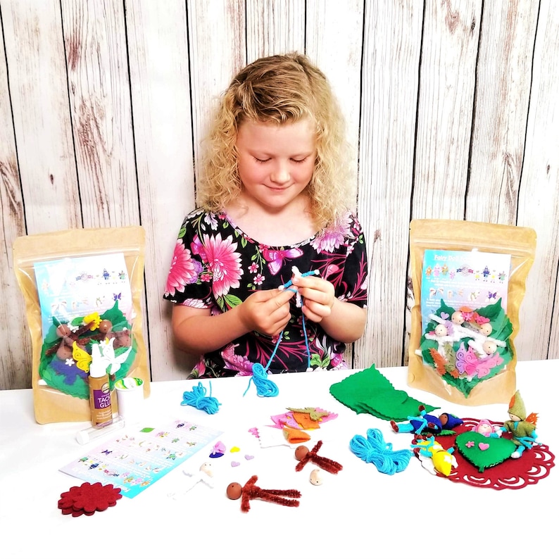 May include: A craft kit for making fairy dolls. The kit includes felt pieces, yarn, pipe cleaners, beads, and instructions. The kit is packaged in two brown bags with clear windows. A young person is shown assembling the fairy doll.
