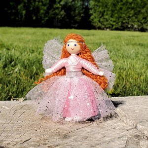 May include: A handmade doll with long, red yarn hair, wearing a pink tulle dress with silver glitter. The doll has a painted face with blue eyes and a pink crown.