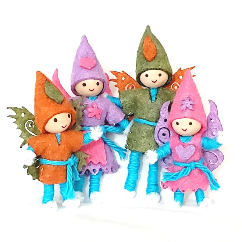 May include: Four felt fairy dolls with wings. The fairies are wearing different colored outfits, including orange, purple, green, and pink. Each fairy has a different colored hat and a blue yarn body.