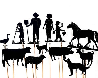 May include: A set of black silhouette figures for shadow puppetry, including a farmer, a woman, a child, a goose, a cow, a pig, a sheep, a dog, a cat, and a horse. The figures are made of black cardboard and are attached to wooden sticks.
