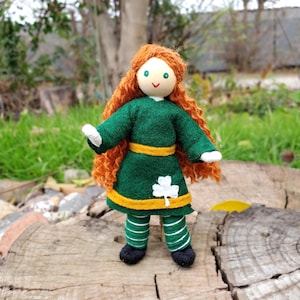 May include: A handmade doll with red curly hair, a green dress with a yellow sash and a white shamrock, and green and white striped pants.