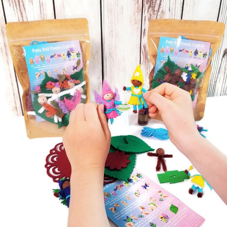 May include: A craft kit for making felt fairy dolls. The kit includes felt pieces in various colors, including pink, blue, green, and yellow. The kit also includes wooden dowels, yarn, and instructions. The kit is packaged in a clear plastic bag with a brown paper backing.