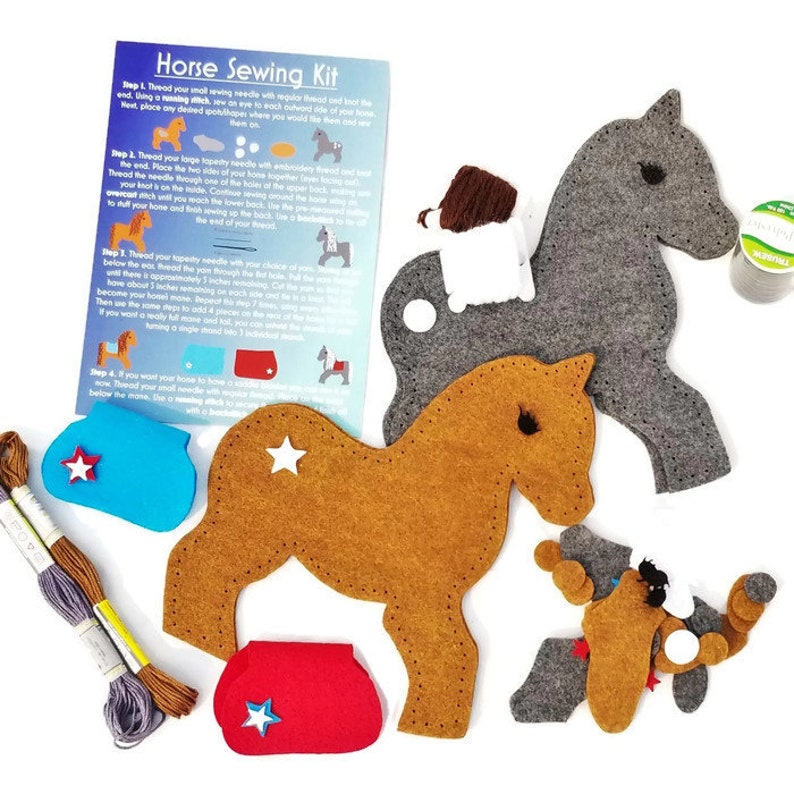 May include: A felt horse sewing kit with instructions. The kit includes two horse shapes, one brown and one gray, along with felt pieces for the horse's mane, tail, and saddle. The kit also includes two spools of thread, a needle, and a star-shaped button.