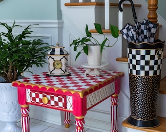May include: A whimsical, hand-painted side table with a red and white checkered top and red and white striped legs. The table features a small drawer with a gold knob and gold accents. A black and white umbrella stand and a decorative clock are nearby.