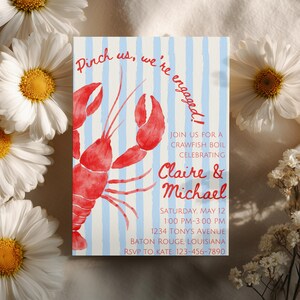May include: An engagement announcement card featuring a red crawfish illustration on a blue and white striped background. The text reads "Pinch us, we're engaged!" and invites guests to a crawfish boil celebrating Claire & Michael.