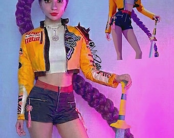 May include: A cosplayer in a yellow cropped jacket with racing-style patches, black shorts, and a long purple braid. She holds a sword with a yellow handle and a purple blade. A cartoon version of the character is also visible.