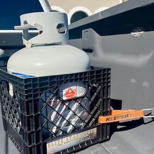 May include: A gray propane tank secured in a black plastic crate with an orange strap. The tank has a white top with the text "TWIST" and "WC475". The crate has the text "ELITE STABLETECH".