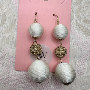 May include: A pair of dangling earrings with a gold-tone hook. Each earring features three decorative elements: a white, spherical, woven ball, a gold-colored, crystal-studded ball, and another white woven ball. The earrings hang from a pink tag.
