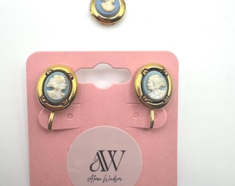 May include: A set of vintage cameo jewelry, including clip-on earrings and a pendant. The earrings and pendant feature a light blue cameo set in a gold-tone frame. The earrings are attached to a pink card with the text "AW Alora Windsor".