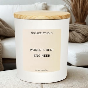 May include: A white candle with a wooden lid. The label reads "SOLACE STUDIO" and "WORLD'S BEST ENGINEER". The candle is a soy wax candle, 9oz.