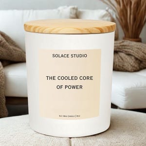 May include: A white soy wax candle with a wooden lid. The label reads "SOLACE STUDIO" and "THE COOLED CORE OF POWER." The candle is 9 oz. and sits on a neutral-toned surface. The overall aesthetic is minimalist and modern.