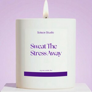 May include: A white, rectangular candle with a lit wick. The candle has a purple label with the text "Solace Studio" and "Sweat The Stress Away." The bottom of the label reads "soy wax candle | 9oz."