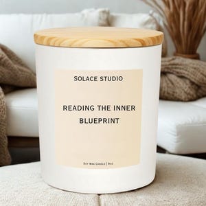 May include: A white candle with a wooden lid. The label reads "SOLACE STUDIO" and "READING THE INNER BLUEPRINT". The candle is a soy wax candle and is 9oz.