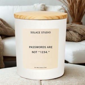 May include: A white soy wax candle with a wooden lid. The candle has a label that reads "SOLACE STUDIO" and "PASSWORDS ARE NOT '1234.'" The candle is 9oz.