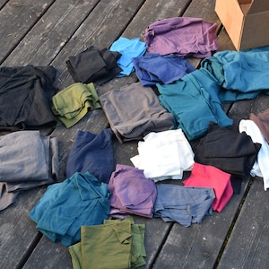 Peut inclure: Un assortiment de chutes de tissu de différentes couleurs, notamment noir, bleu, vert, rouge et blanc, disposées sur une surface en bois. Les chutes de tissu sont pliées et empilées, et certaines sont étalées.