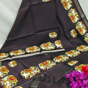 May include: Dark brown saree with a repeating pattern of white elephants adorned with red and gold details. The border features a gold and black geometric design. The fabric is draped, showcasing the intricate design and texture.
