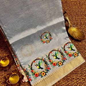 May include: A light gray textile with a hummingbird and floral design. The fabric has a subtle striped texture and a gold border. The design features colorful hummingbirds within floral wreaths, creating a vibrant contrast.