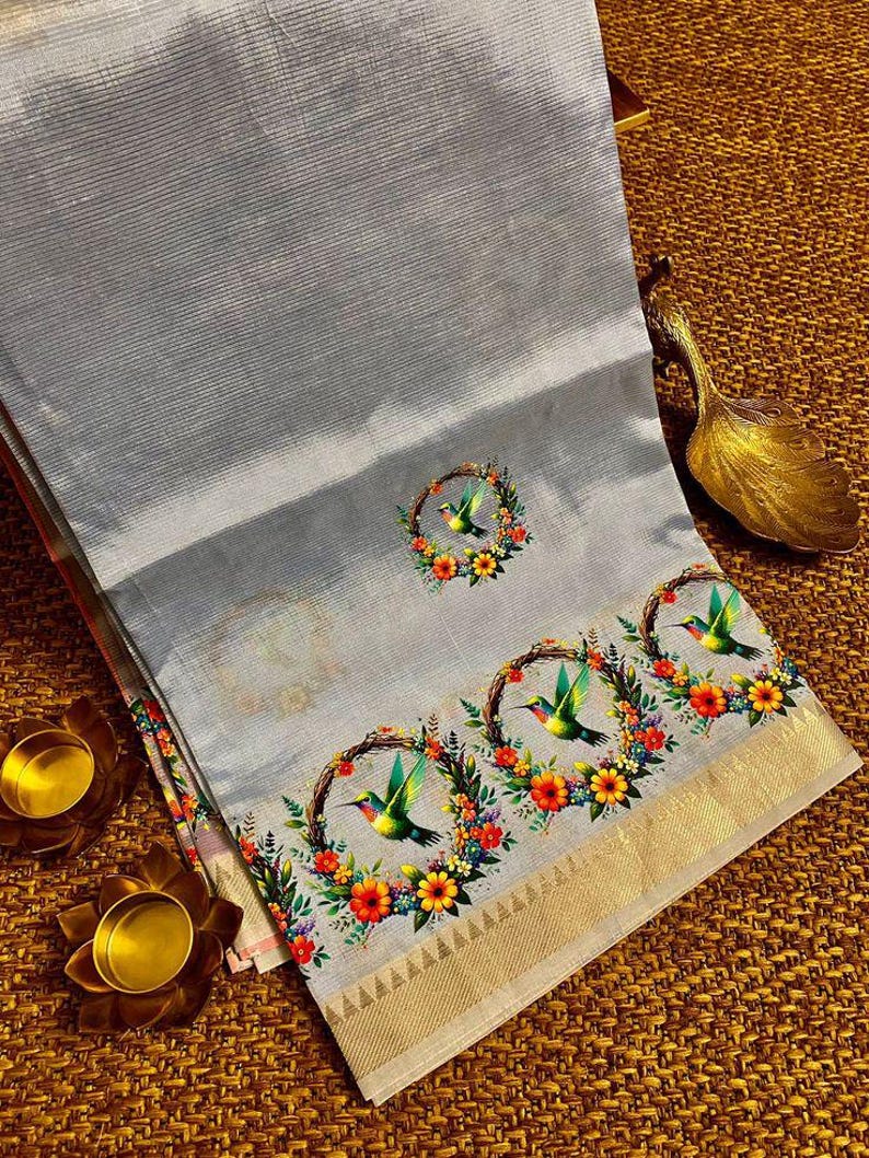 May include: A light gray textile with a hummingbird and floral design. The fabric has a subtle striped texture and a gold border. The design features colorful hummingbirds within floral wreaths, creating a vibrant contrast.