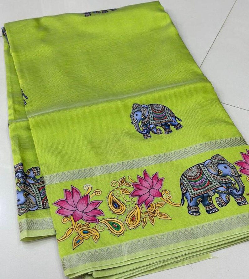 May include: A lime green textile with a decorative border featuring elephants, lotus flowers, and paisley designs. The elephants are blue with detailed patterns. The border has a silver trim.