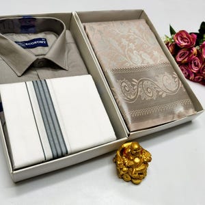 Könnte beinhalten: Ein Geschenkset mit einem grauen Hemd, einem weißen Taschentuch mit grauen Streifen und einem gemusterten Schal, alles in einer weißen Box präsentiert. Eine kleine goldene Buddha-Statue und ein Strauß rosa Rosen sind ebenfalls zu sehen.
