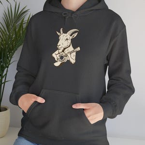May include: Dark gray hoodie featuring a tan illustration of a goat playing a guitar. The guitar has the text "Billy Strings" on it. The hoodie has a front pocket and a hood with a drawstring.