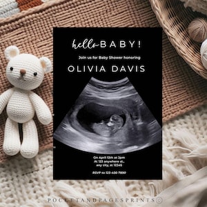 May include: A black baby shower invitation with the text "hello BABY!" and an ultrasound image. The invitation includes the name "OLIVIA DAVIS" and event details. A white crocheted teddy bear is on the left. The background is neutral.