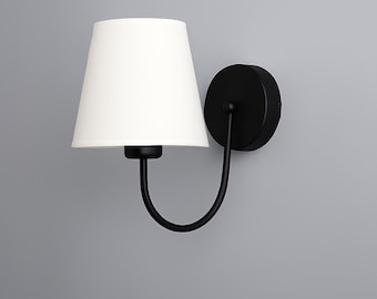 May include: A modern wall sconce with a white lampshade and a black metal frame. The lampshade is cone-shaped, and the fixture is mounted on a round black base. The curved arm connects the shade to the base, creating a sleek, minimalist design.
