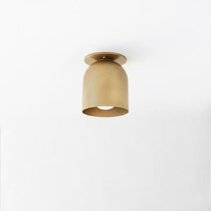 May include: A brass-colored, dome-shaped ceiling light fixture. The light has a rounded, bell-like shade and a circular base. The fixture is mounted on a white ceiling, providing a warm, ambient glow.