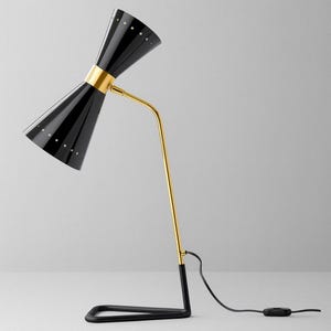 May include: A black and gold desk lamp with an hourglass-shaped shade. The lamp has a gold-coloured arm and accents, a black base, and a power cord with an on/off switch. The shade has small, evenly spaced white dots.