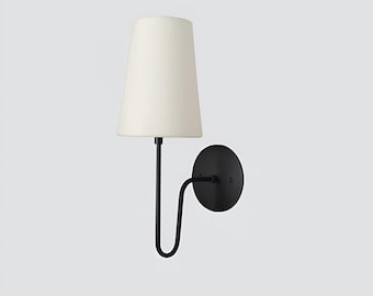 May include: A modern wall sconce with a black metal frame and a cream-colored lampshade. The sconce features a circular base, a curved arm, and a tapered lampshade. The design is minimalist and suitable for various interior styles.