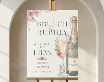 May include: A rectangular sign on a wooden easel featuring the text Brunch & Bubbly, Welcome to Lily's Bridal Shower, March 7th 2026 at 3PM. The design includes a watercolor illustration of a champagne bottle and a glass with pink floral accents.
