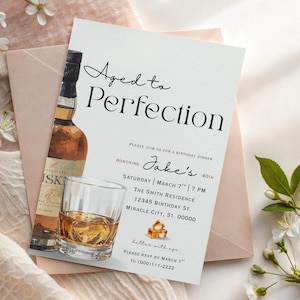 Puede incluir: Invitación de cumpleaños "Aged to Perfection" con una botella de whisky y un vaso de whisky. La invitación incluye el texto "Jake's 40th" y los detalles del evento. El diseño está sobre un fondo blanco con un sobre rosa.
