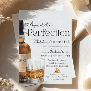 May include: A rectangular birthday invitation card featuring a whiskey bottle and a glass of whiskey with ice cubes. The text reads: Aged to Perfection, Shhh...it's a surprise!, Please join us for a birthday dinner honoring Jake's 40th, March 7th, 7 PM.