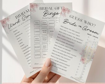 May include: Three white paper bridal shower game cards featuring floral accents. The cards include Bridal Gift Bingo, Bridal Word Scramble, and Guess Who? Bride or Groom. Each card has black text, lines for names, and checkboxes for game play.