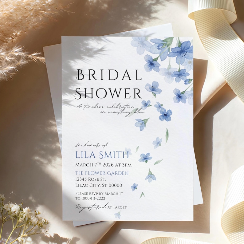 May include: A white invitation for a bridal shower with blue floral accents. The text reads "BRIDAL SHOWER" and includes event details such as the date, time, and location. The invitation is decorated with watercolor-style blue flowers.