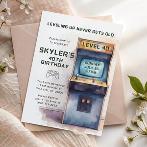 May include: A rectangular birthday invitation card featuring a watercolor-style arcade cabinet illustration. Text reads: LEVELING UP NEVER GETS OLD, PLEASE JOIN US TO CELEBRATE SKYLER'S 40TH BIRTHDAY, SUNDAY JULY 26 @7PM, THE SMITH RESIDENCE, AND RSVP DETAILS.