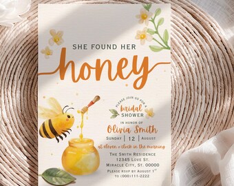 May include: Bridal shower invitation with a bee theme. The invitation features the words "She found her honey" in orange script. A cartoon bee is shown with a honey dipper pouring honey into a jar. The invitation includes the date, time, and location.