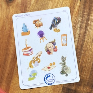 Puede incluir: Una hoja de pegatinas blanca titulada Wizard's Rest que presenta varias ilustraciones que incluyen un cristal, un cofre del tesoro, un cuervo, una bola de cristal, libros con una vela, una calavera, un reloj de arena, una pluma y un gato.