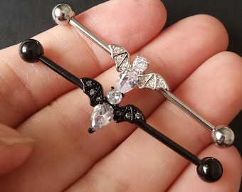 May include: Two industrial barbells. One is black with a bat design and the other is silver with a bat design. Each bat has a clear, teardrop-shaped gem in the centre and is adorned with small, clear gems.