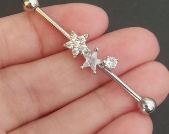 May include: A silver industrial barbell earring with two star charms and a single round charm. The stars are encrusted with clear crystals. The barbell has a ball on each end.