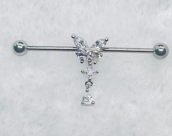 May include: A silver industrial barbell earring with a butterfly design and clear crystals. The butterfly is the central feature, with three dangling crystals below. The barbell has a ball at each end. The crystals sparkle.
