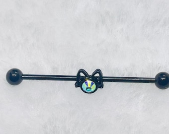May include: Black industrial barbell with a cat-shaped charm. The charm has a colourful iridescent gem, and the barbell has a black ball on each end. This body jewellery is designed for ear piercings.