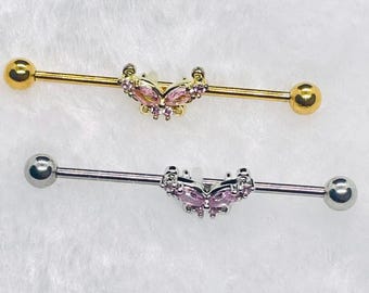 May include: Two industrial barbells. One is gold-toned with pink gem butterfly and gold balls. The other is silver-toned with a pink gem butterfly and silver balls. Both are on a white background.
