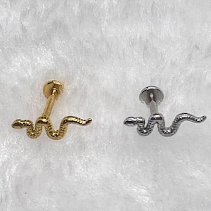 May include: Two flat-back earrings with a snake design. One earring is gold-colored, and the other is silver-colored. The snake design is a stylized, winding shape.