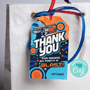 Könnte beinhalten: Ein blaues und oranges Dankeschön-Etikett mit einer Nerf-Pistole aus dem Cartoon, Zielkreisen und Sternen. Der Text lautet "Vielen Dank, dass du meine Party zu einem KNALL gemacht hast! -Ethan".