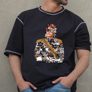 May include: Black short-sleeved t-shirt with a collage portrait of a person wearing sunglasses and a military-style jacket with gold detailing. The shirt has white stitching on the sleeves and neckline.